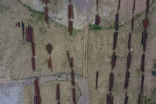 Aerial view of industrial metal pipes arranged in rows on a dry, grassy field in Englewood, Colorado, United States.