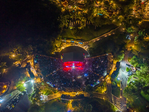 Aerial view of the Altos de Chavon Amphitheatre at night, illuminated with vibrant stage lights, surrounded by lush gardens and parking areas in La Romana, La Romana, Dominican Republic.
