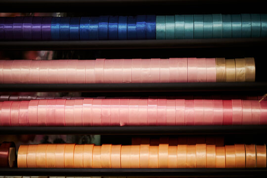 Close up view of colorful satin ribbon spools neatly organized on shelves. Image suitable for DIY craft tutorials, textile industry, gift wrapping marketing