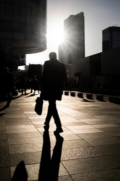 Businessman walking in backlight between office towers in La Defense district of Paris France showing contemporary urban business life