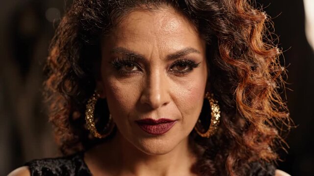 Close-up portrait of a glamorous woman with curly hair and bold makeup.