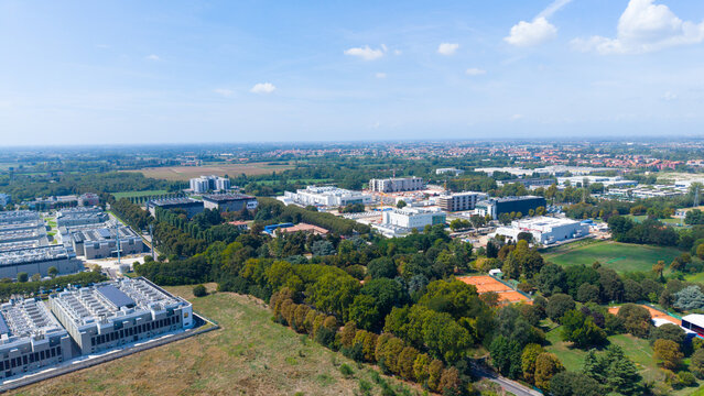 Aerial view of a large data center cluster with industrial buildings, cooling systems, and surrounding green spaces in Castelletto, Lombardia, Italy.