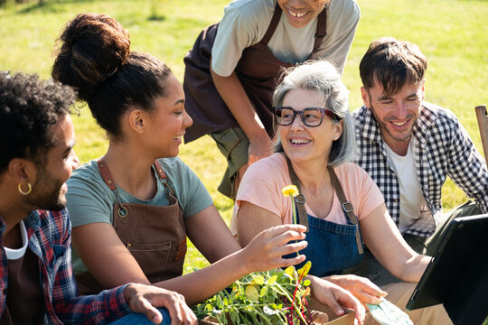 Group of smiling friends sharing gardening hobby at community farm