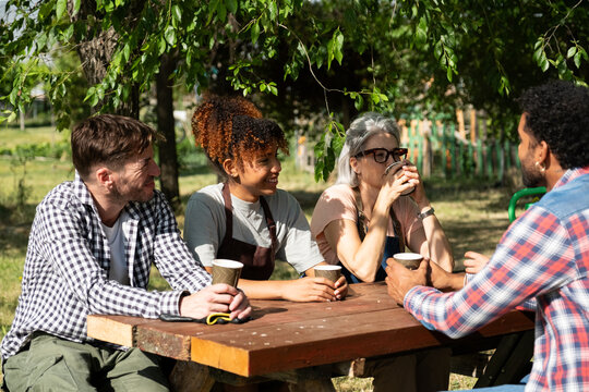 Diverse friends sitting around a picnic table, drinking coffee, and having a lively conversation outdoors