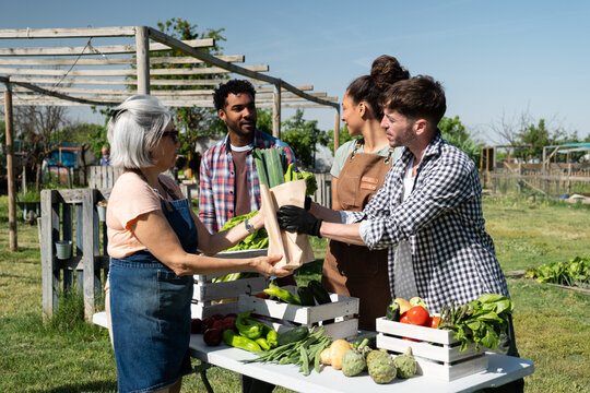 Group of diverse people exchanging vegetables at an outdoor farmers market stall