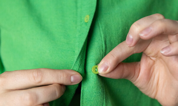 Close-up of hands buttoning a vibrant green linen shirt.