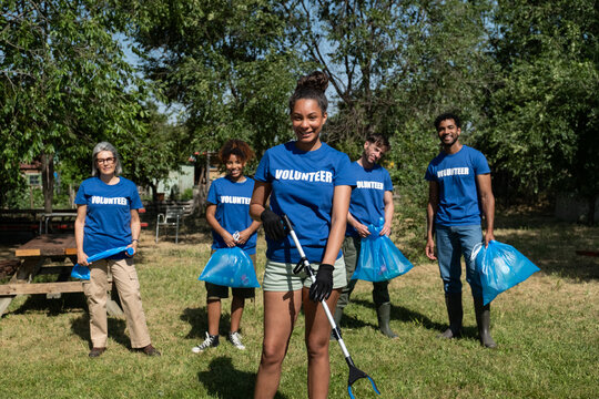 Diverse volunteers standing outdoors with garbage bags and grabbers after cleaning