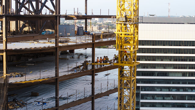 Aerial view of a construction site with a yellow tower crane, steel beams, and workers on a high-rise building under construction in Cambridge, Massachusetts, United States.