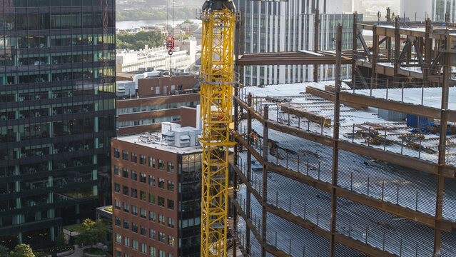 Aerial view of a construction site with a prominent yellow tower crane and steel framework rising amidst urban buildings in Cambridge, Massachusetts, United States.