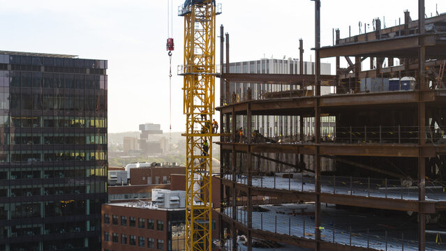 Aerial view of a construction site featuring a tall yellow crane and a steel frame building under development in Cambridge, Massachusetts, United States.