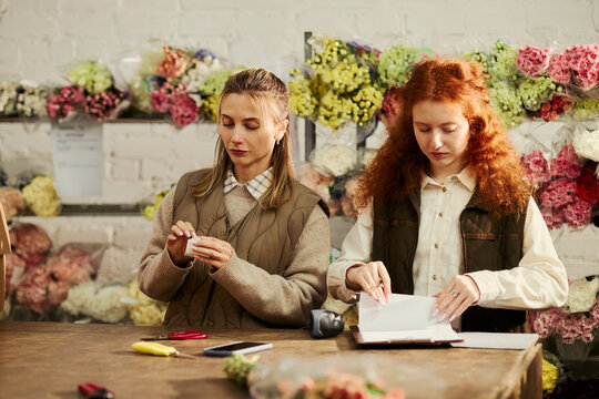 Two young Caucasian female florists preparing orders and checking clipboard in flower shop. Commercial use includes small business management and retail marketing