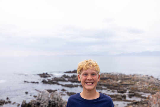 smiling boy in stormy late afternoon light on rocky coastline of DeKelders, South Africa