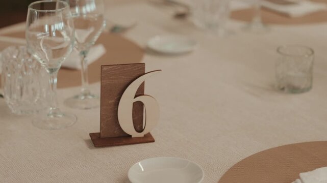 Wooden table number 6 standing on a neatly set dining table with empty glasses and plates, organizing guests for an event