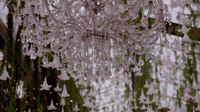 Crystal chandelier sparkling with shimmering drops, suspended amidst white bell shaped decorations and soft lights, creating an elegant event atmosphere