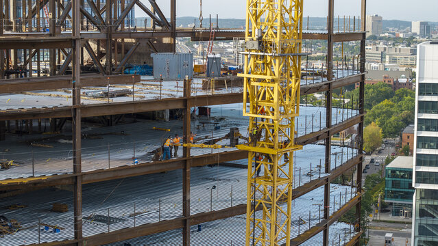 Aerial view of a construction site with a steel frame and yellow tower crane with workers in safety vests on the metal decking in Cambridge, Massachusetts, United States.