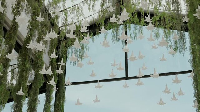 White bell shaped flowers and green vines hanging from a glass ceiling, creating elegant decor for a special event or wedding