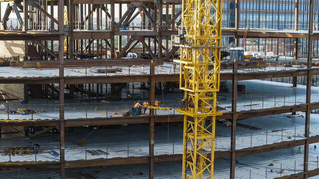 Aerial view of a construction site featuring a prominent yellow tower crane and workers on steel beams in Cambridge, Massachusetts, United States.