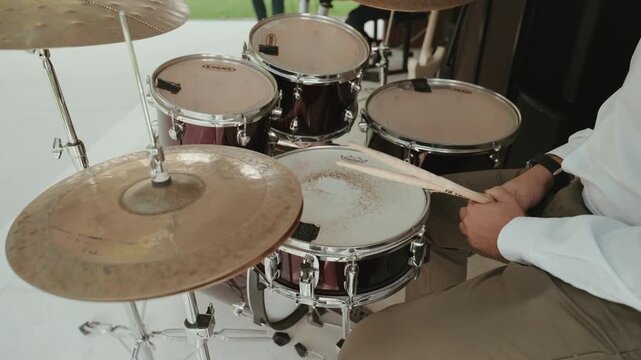Musician's hands playing drum kit with drumsticks, hitting snare drum and cymbal, creating rhythm and music