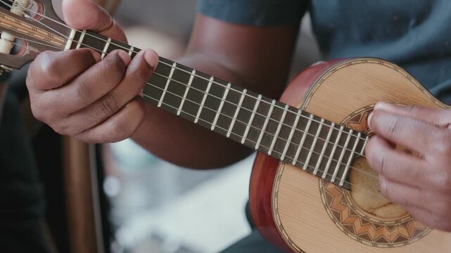 Person playing a traditional Cavaquinho string instrument with their hands, showing the fretboard and musical performance