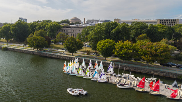 Aerial view of colorful sailboats docked at a pier on the Charles River with the MIT Great Dome in the background, near trees in Cambridge, Massachusetts, United States.