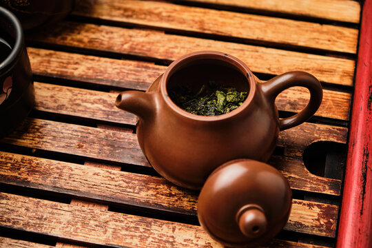Brown ceramic teapot with dried green tea on wooden surface