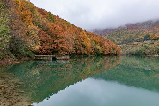 The Autumn Lake Surrounded by Colorful Foliage and Misty Mountains