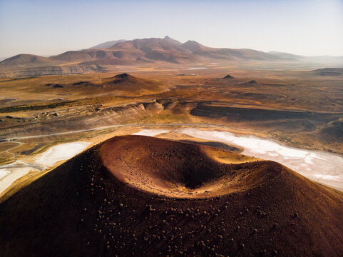 Aerial view of the volcanic crater and caldera cone of Lake Meke surrounded by arid landscape and salt flats with distant mountains on the horizon in Karapinar, Konya, Turkiye.