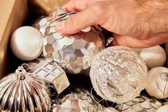 Hand taking shiny silver Christmas ornaments out of a storage box
