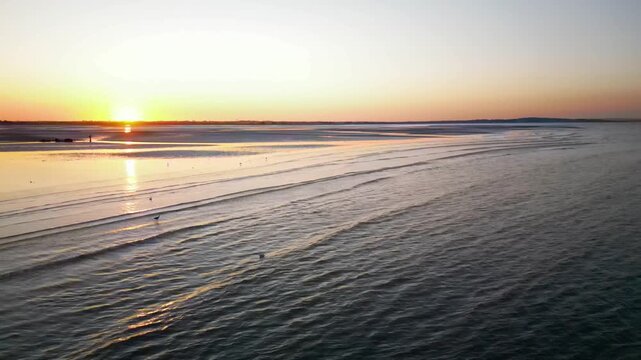 Aerial drone view flying over gentle sea waves and sandy beach at sunset in Howth, Ireland