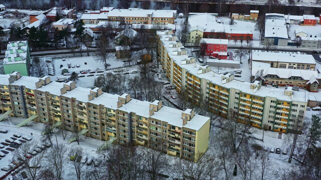 Aerial view of multi-story residential apartment buildings surrounded by snow-covered trees and parking lots in a winter landscape in Latvija.