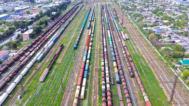 Aerial view of a large railway yard with numerous parallel tracks filled with freight train cars, surrounded by urban residential areas and green spaces in Tbilisi, Tbilisi, Georgia.