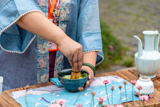 Woman wearing a traditional light blue Chinese dress preparing tea using a traditional tea-making method in a Chinese garden in Huishan Ancient Town, Wuxi, China.