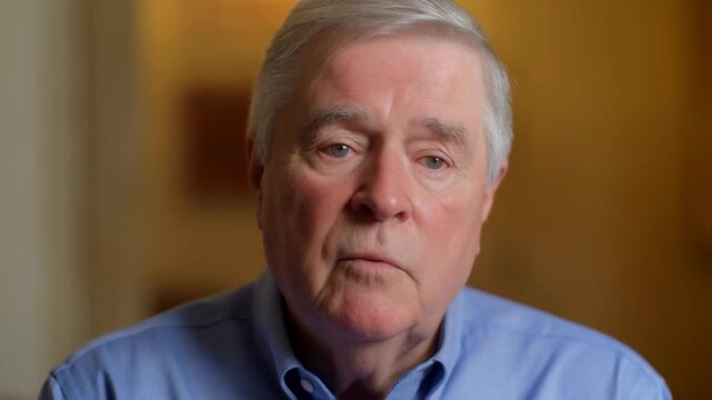 Older man speaking directly to camera in a warmly lit indoor interview portrait. Documentary production, testimonial campaigns, and journalism segments.