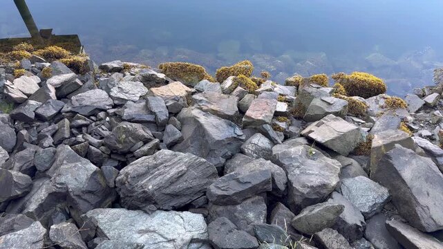 High angle textured b-roll showing large fractured volcanic rocks and boulders piled along a coastal water embankment.