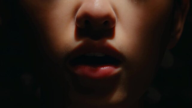 Extreme close-up of an adult human mouth moving while speaking or breathing in dramatic warm low-key. Film and television transitions, communication campaigns.
