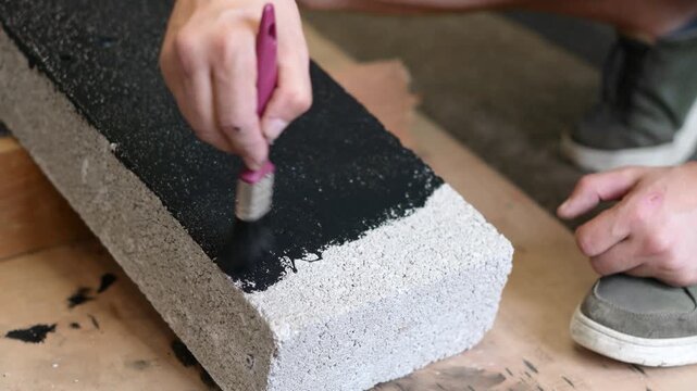 Man using a brush to paint the exposed edge of a concrete building block black