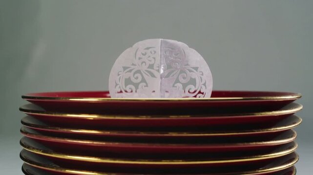 Pulling back camera revealing laser-cut ornament on stacked red plates on table, showing gold rims