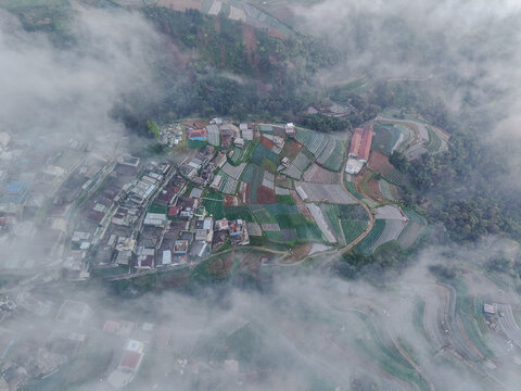 Aerial view of Nepal Van Java, a village nestled on the slopes of Mount Sumbing with terraced vegetable fields and houses shrouded in morning mist in Magelang, Central Java, Indonesia.