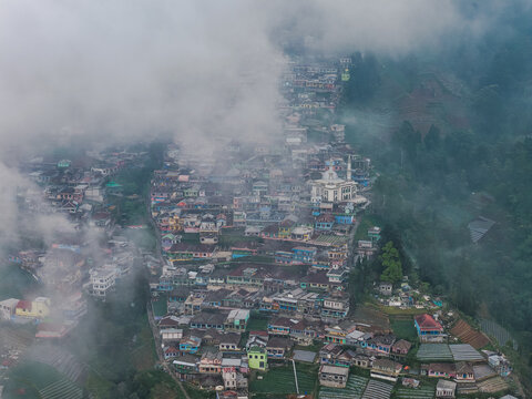 Aerial view of Nepal Van Java village with colorful houses nestled on the terraced slopes of Mount Sumbing surrounded by mist in Magelang, Central Java, Indonesia.