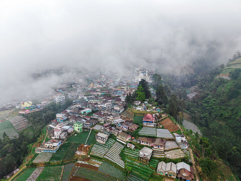 Aerial view of Nepal Van Java village with colorful houses nestled on the terraced slopes of Mount Sumbing surrounded by mist in Magelang, Central Java, Indonesia.