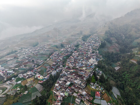 Aerial view of Nepal Van Java village nestled on the slopes of Mount Sumbing with terraced vegetable fields and dense housing in Magelang, Central Java, Indonesia.