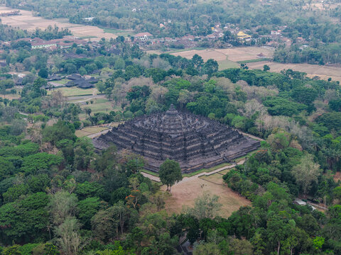 Aerial view of Borobudur Temple, a massive ancient Buddhist monument, surrounded by lush green trees and tropical vegetation in Magelang, Jawa Tengah, Indonesia.