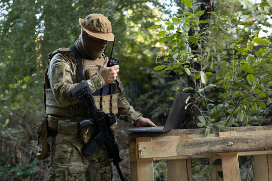A soldier works on a laptop and a two-way radio in the field while carrying out a mission.