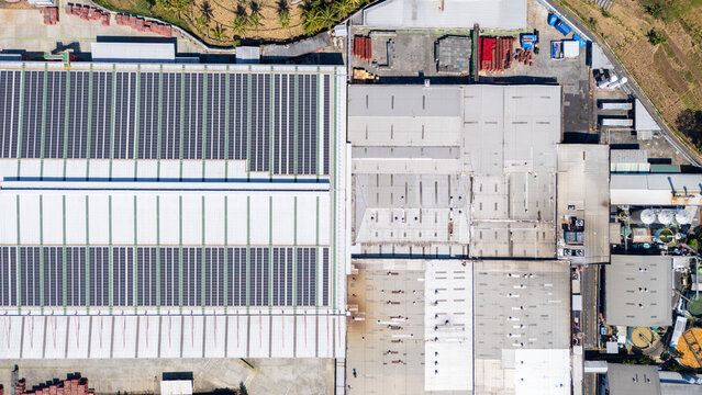 Aerial view of an industrial facility featuring a large solar panel array on the roof, surrounded by metal roofing and industrial infrastructure in Salatiga, Central Java, Indonesia.