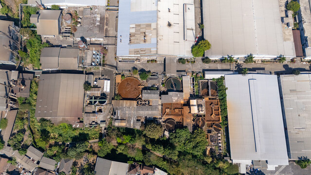 Aerial view of an industrial facility with circular processing tanks and large warehouse buildings surrounded by lush greenery in Salatiga, Central Java, Indonesia.