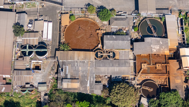 Aerial view of an industrial wastewater treatment plant featuring large circular sedimentation tanks and factory buildings with corrugated metal roofs in Salatiga, Central Java, Indonesia.