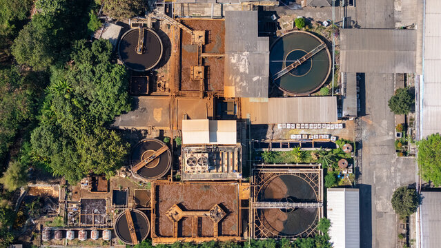 Aerial view of an industrial wastewater treatment facility with circular sedimentation tanks and rectangular basins surrounded by trees in Salatiga, Central Java, Indonesia.