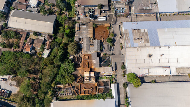 Aerial view of an industrial wastewater treatment plant featuring circular sedimentation tanks and large warehouse buildings surrounded by lush trees in Salatiga, Central Java, Indonesia.
