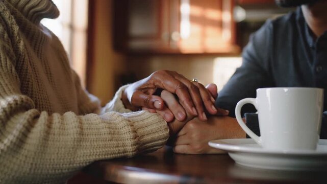 Placing senior couple clasping hands at home seeking calm knit sweater henley gold ring coffee cup