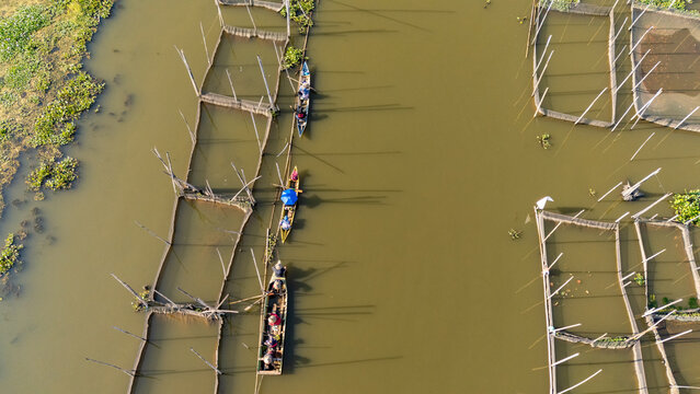 Aerial view of traditional fish farming nets and small wooden boats with people navigating the calm river waters in Salatiga, Central Java, Indonesia.